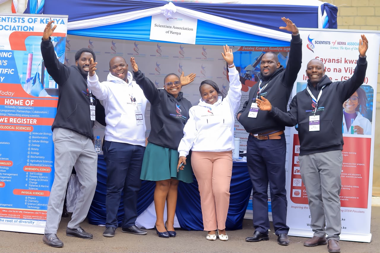 Energetic young SCOKA members in branded hoodies celebrating at an outdoor science exhibition booth